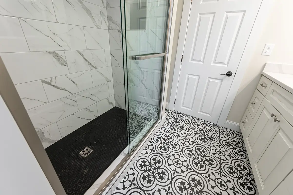 Beautifully remodeled bathroom with white marble shower, walls, glass, shower, door, and black and white tiled floor