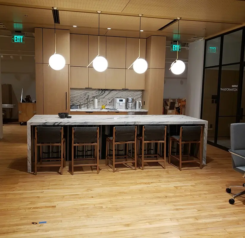 Newly remodeled commercial office kitchen space with four pendant lights and a marble table with chairs