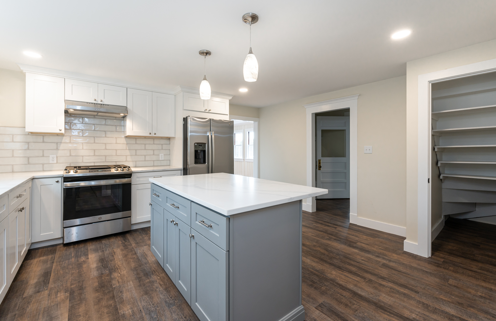 Beautifully remodeled kitchen with white marble countertops, white cabinets, stainless steel appliances, hardwood floors, white tile backsplash
